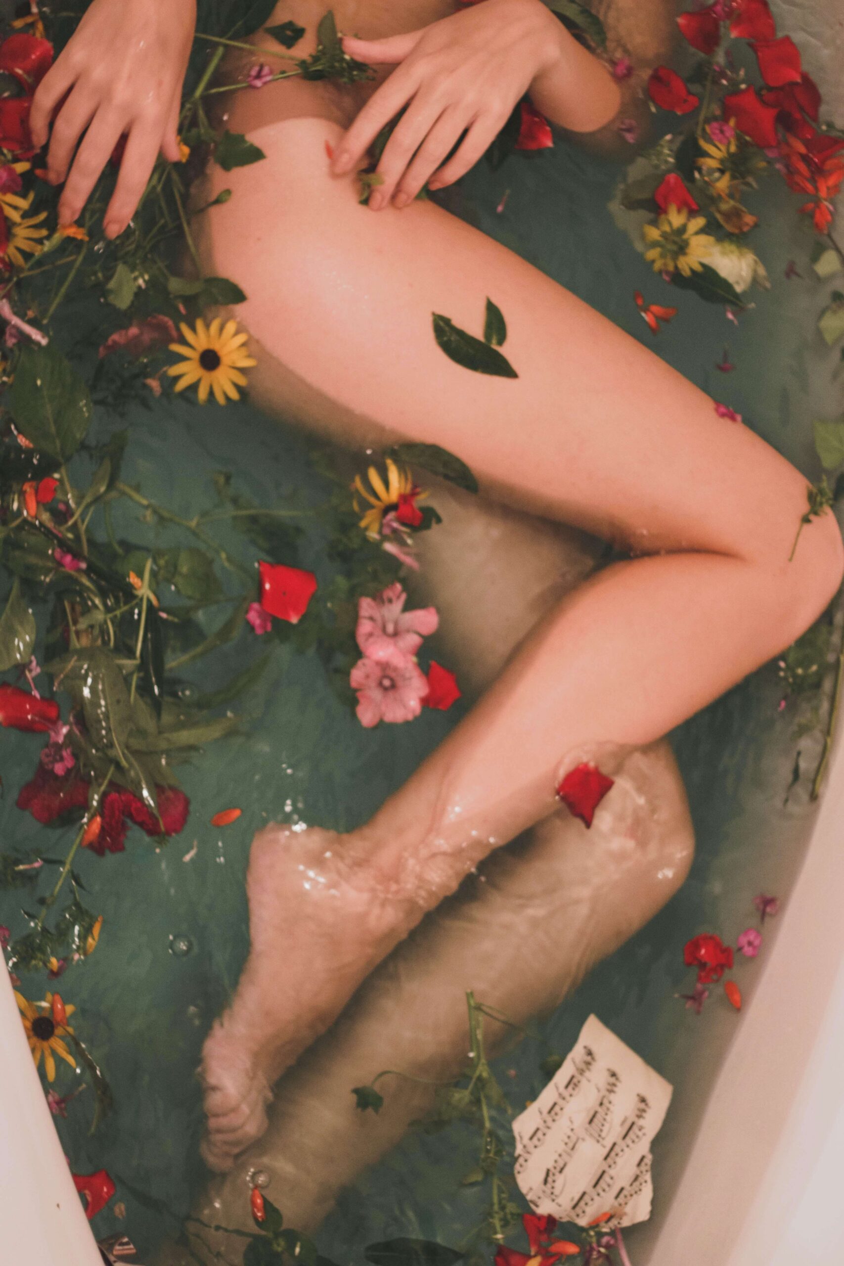 women in a bath surrounded by floating petals, looks serene and she's taking care of herself
